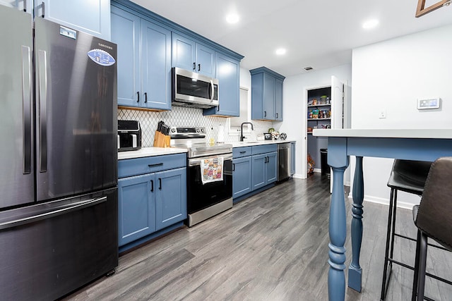 kitchen featuring blue cabinetry, backsplash, dark hardwood / wood-style flooring, and stainless steel appliances