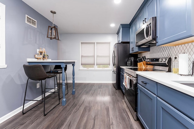 kitchen with appliances with stainless steel finishes, backsplash, dark wood-type flooring, blue cabinetry, and pendant lighting