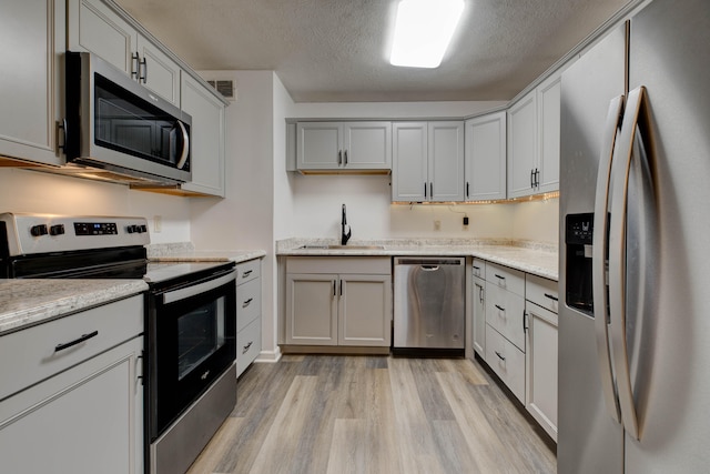 kitchen featuring light stone countertops, a textured ceiling, stainless steel appliances, sink, and light hardwood / wood-style flooring