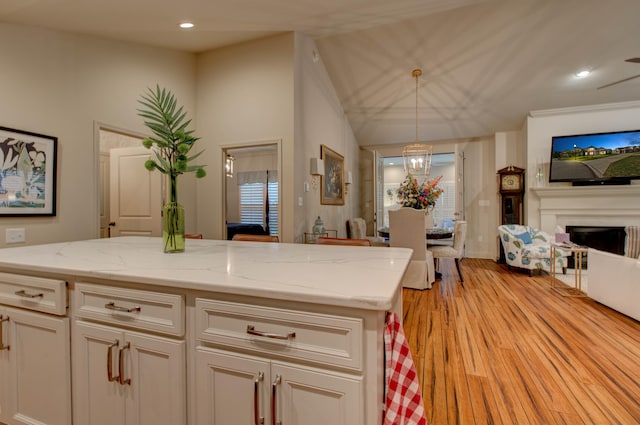 kitchen featuring light stone countertops, light wood-type flooring, vaulted ceiling, decorative light fixtures, and white cabinets