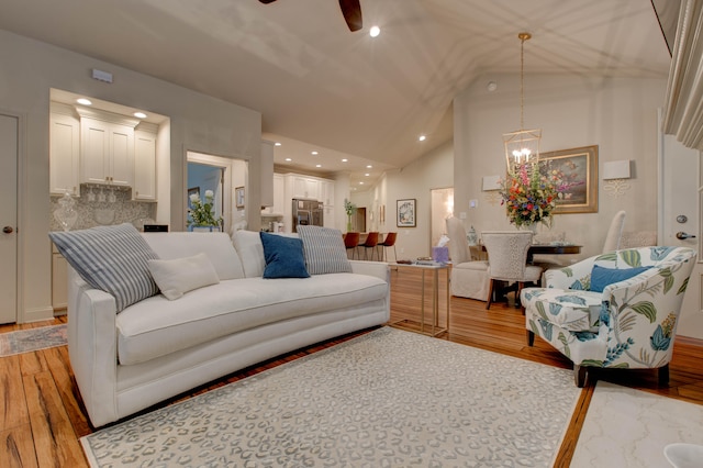 living room featuring ceiling fan with notable chandelier, light wood-type flooring, and high vaulted ceiling