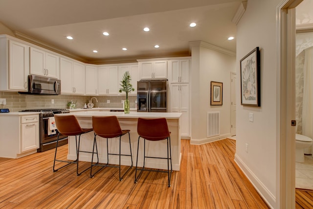 kitchen with white cabinetry, light hardwood / wood-style flooring, a breakfast bar, a center island with sink, and appliances with stainless steel finishes