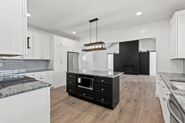 kitchen featuring appliances with stainless steel finishes, white cabinets, a kitchen island, decorative light fixtures, and a barn door