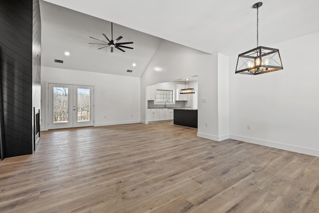 unfurnished living room featuring french doors, sink, high vaulted ceiling, light wood-type flooring, and ceiling fan with notable chandelier