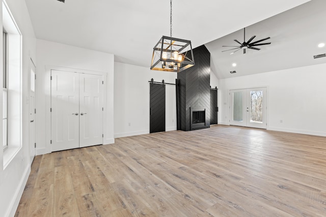 unfurnished living room with ceiling fan, a barn door, high vaulted ceiling, and light hardwood / wood-style flooring