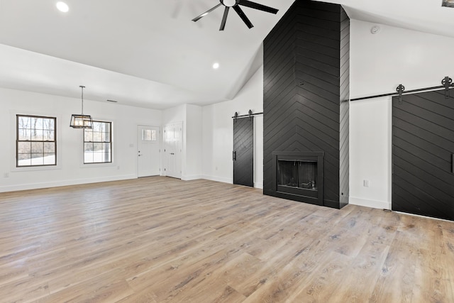 unfurnished living room featuring high vaulted ceiling, a barn door, ceiling fan, and light wood-type flooring