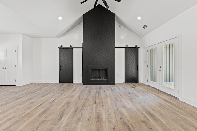 unfurnished living room featuring a barn door, lofted ceiling, and light hardwood / wood-style flooring