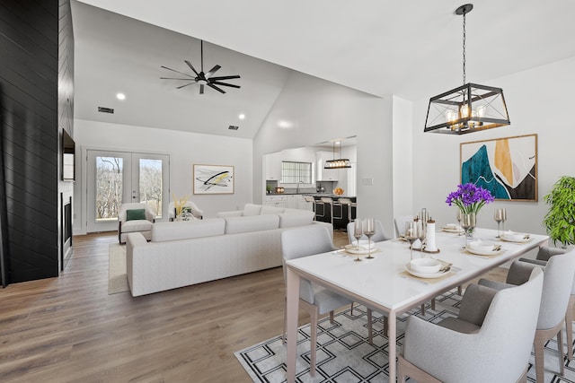 dining area with french doors, high vaulted ceiling, ceiling fan with notable chandelier, and hardwood / wood-style floors