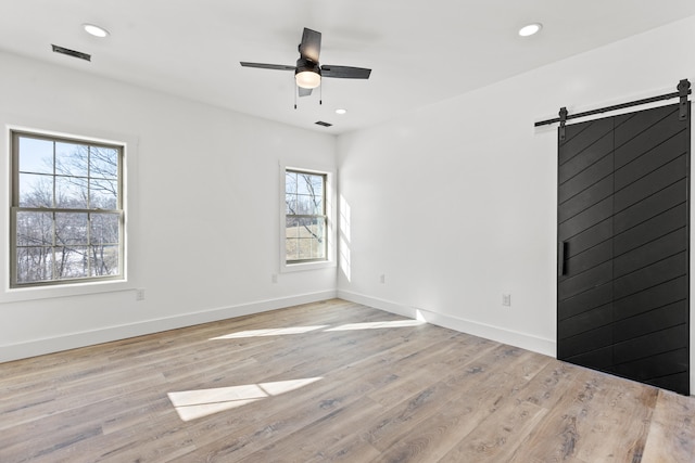 empty room with plenty of natural light, a barn door, ceiling fan, and light wood-type flooring