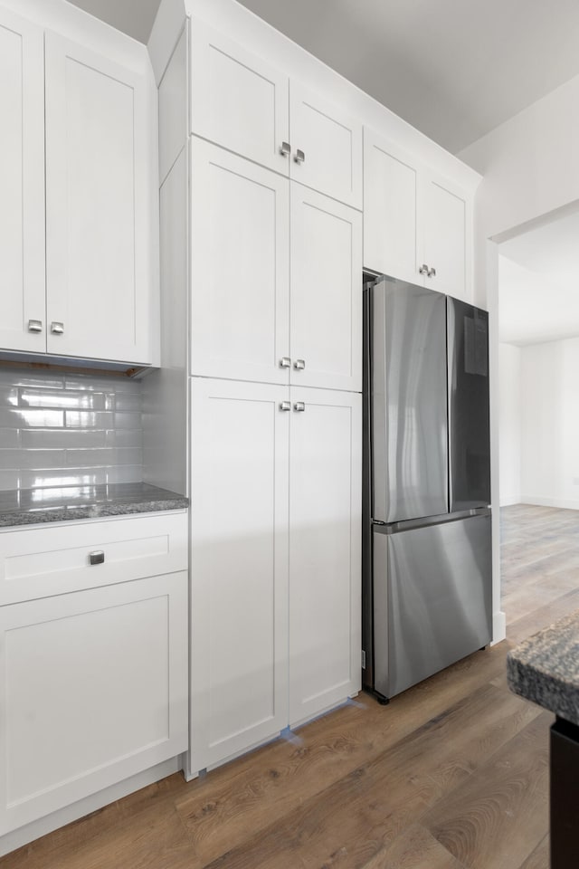 kitchen featuring white cabinetry, dark stone countertops, stainless steel refrigerator, dark hardwood / wood-style flooring, and decorative backsplash