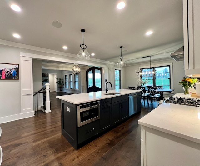 kitchen with a kitchen island with sink, sink, hanging light fixtures, appliances with stainless steel finishes, and dark hardwood / wood-style flooring