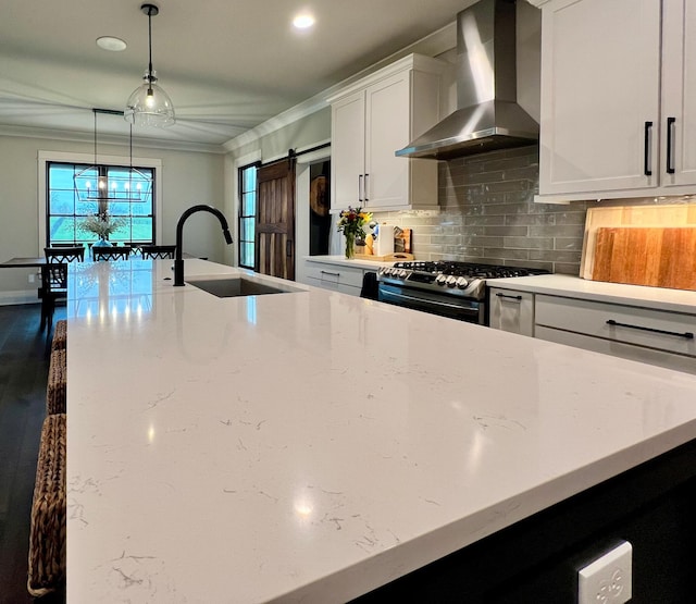 kitchen featuring a barn door, stainless steel range oven, light stone counters, and wall chimney range hood