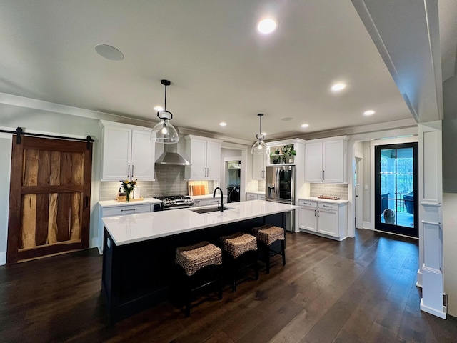 kitchen with sink, stainless steel appliances, a barn door, decorative light fixtures, and a kitchen island with sink