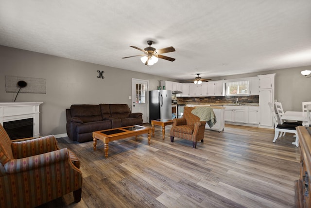 living room with ceiling fan, sink, a textured ceiling, and light wood-type flooring