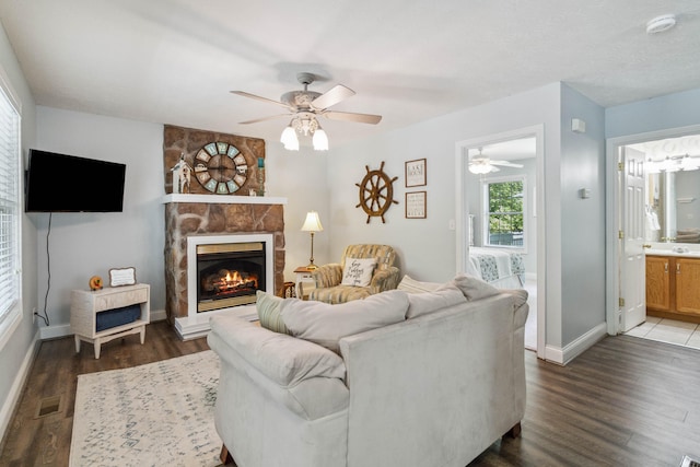 living room featuring dark hardwood / wood-style flooring, a stone fireplace, and ceiling fan