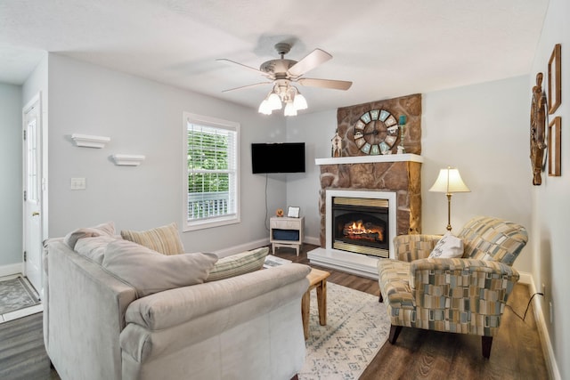 living room featuring dark hardwood / wood-style floors, ceiling fan, and a stone fireplace