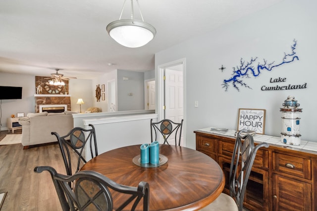 dining area featuring ceiling fan, wood-type flooring, and a fireplace