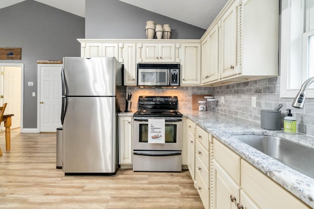 kitchen featuring stainless steel appliances, light stone counters, light hardwood / wood-style flooring, cream cabinets, and lofted ceiling