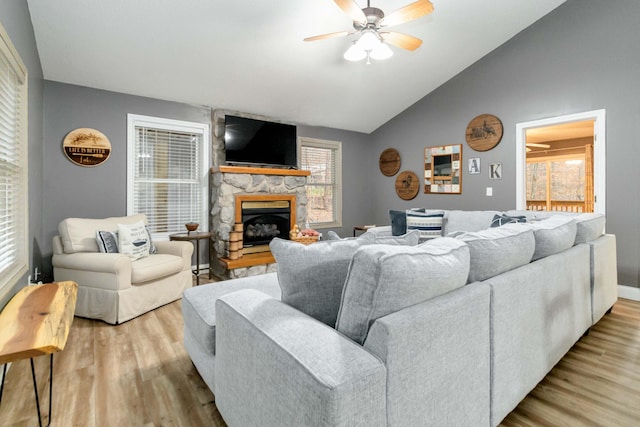 living room with ceiling fan, vaulted ceiling, a stone fireplace, and light hardwood / wood-style flooring