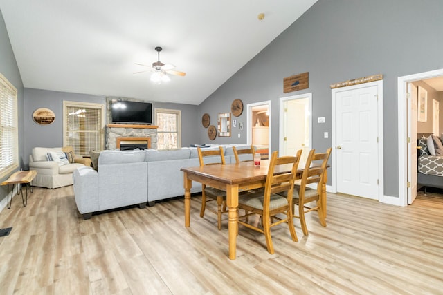 dining space featuring ceiling fan, light wood-type flooring, a fireplace, and high vaulted ceiling