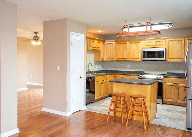 kitchen with appliances with stainless steel finishes, a center island, ceiling fan, decorative backsplash, and sink