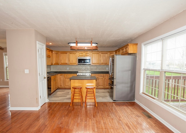 kitchen featuring a center island, a kitchen bar, light wood-type flooring, backsplash, and appliances with stainless steel finishes