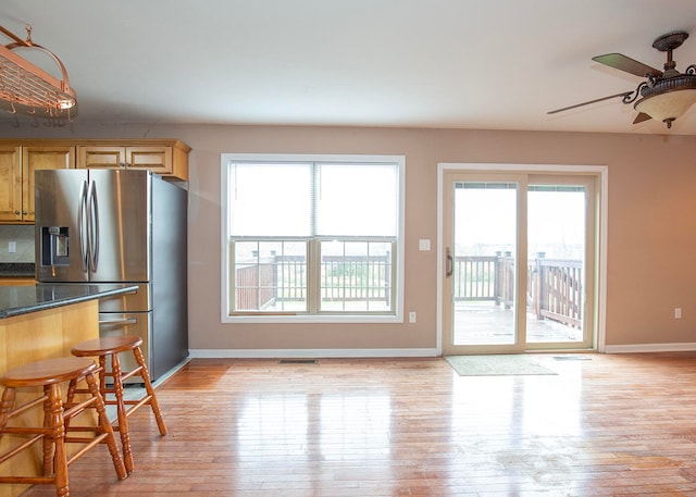 kitchen with light brown cabinets, ceiling fan, light hardwood / wood-style floors, dark stone counters, and stainless steel refrigerator with ice dispenser