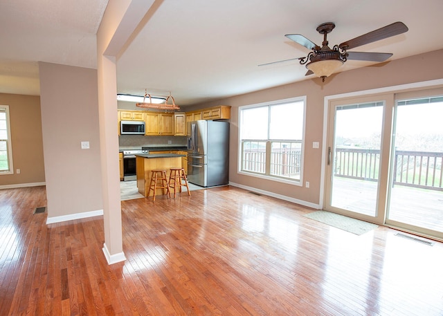 kitchen featuring a kitchen breakfast bar, stainless steel appliances, light wood-type flooring, ceiling fan, and tasteful backsplash