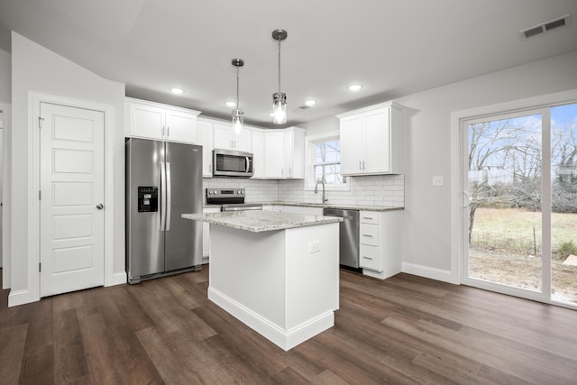 kitchen featuring stainless steel appliances, decorative light fixtures, a center island, and white cabinets