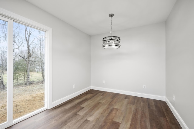 unfurnished dining area featuring dark wood finished floors, baseboards, and an inviting chandelier