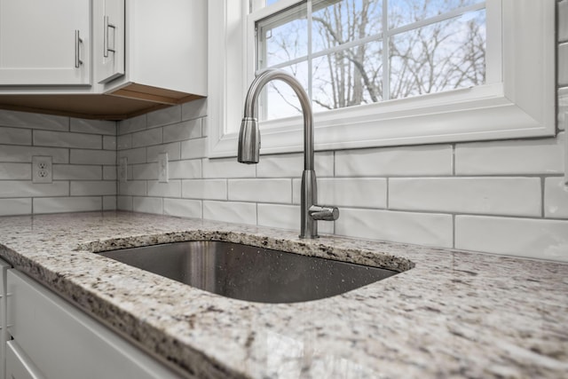 room details featuring sink, white cabinets, decorative backsplash, and light stone counters