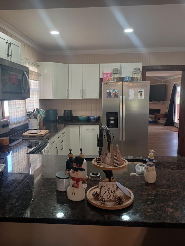 kitchen with white cabinetry, stainless steel appliances, ornamental molding, dark stone countertops, and hardwood / wood-style flooring