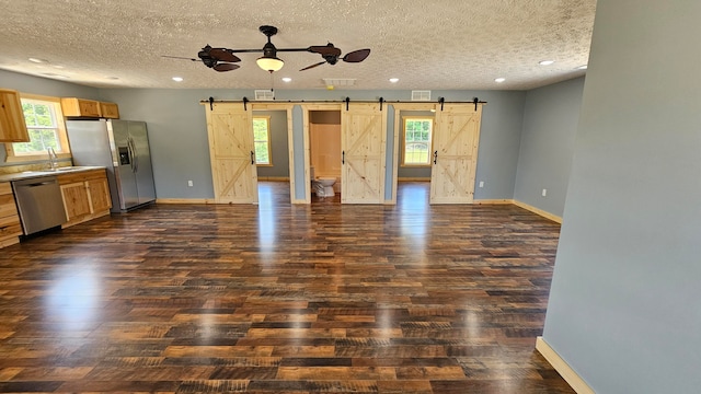 unfurnished living room featuring a barn door, dark hardwood / wood-style flooring, a healthy amount of sunlight, and a textured ceiling