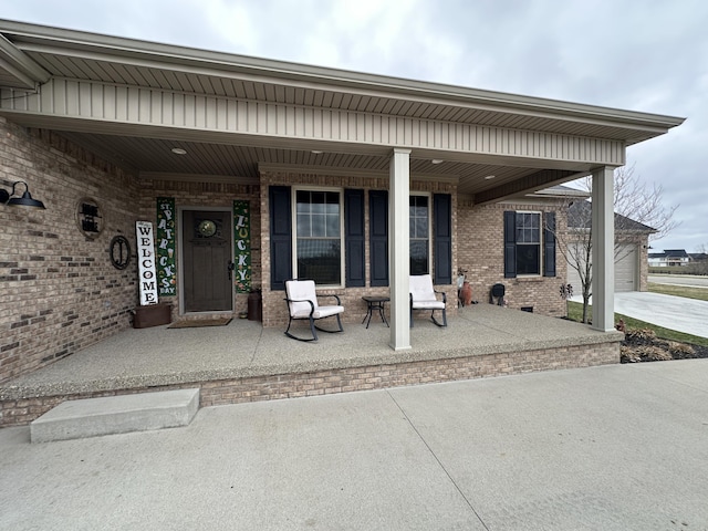 doorway to property featuring brick siding, a porch, and driveway