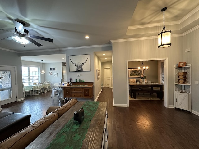 living room with dark wood finished floors, crown molding, ceiling fan with notable chandelier, and baseboards