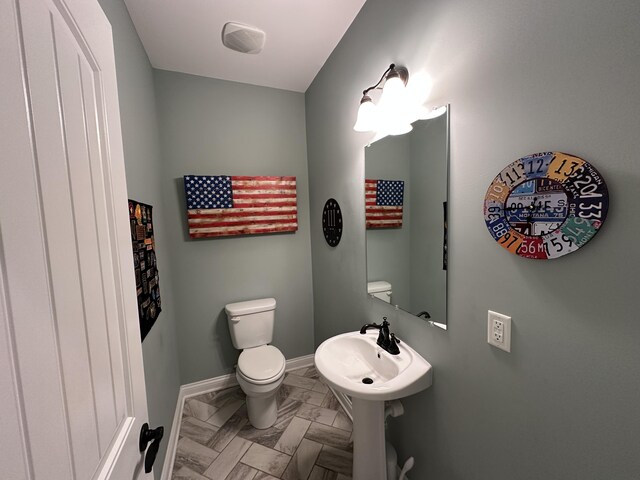 half bathroom with baseboards, toilet, and marble finish floor