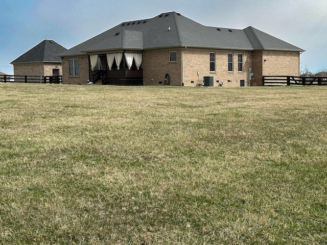 rear view of house with cooling unit, a lawn, brick siding, and fence