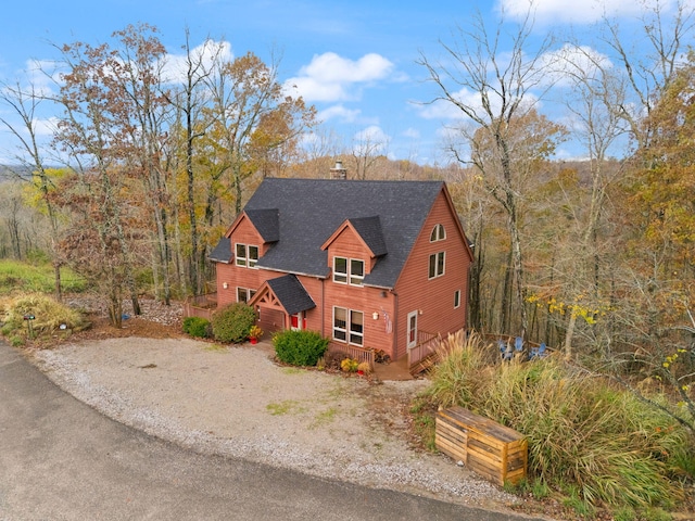 view of front facade with a shingled roof, driveway, and a chimney