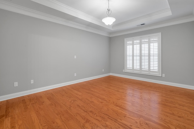 spare room featuring a raised ceiling, ornamental molding, and light hardwood / wood-style flooring