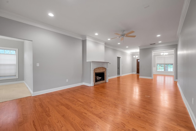 unfurnished living room with ceiling fan with notable chandelier, light hardwood / wood-style floors, ornamental molding, and a wealth of natural light