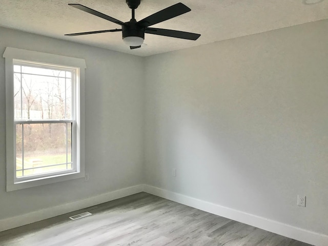 spare room featuring ceiling fan, a healthy amount of sunlight, light hardwood / wood-style floors, and a textured ceiling