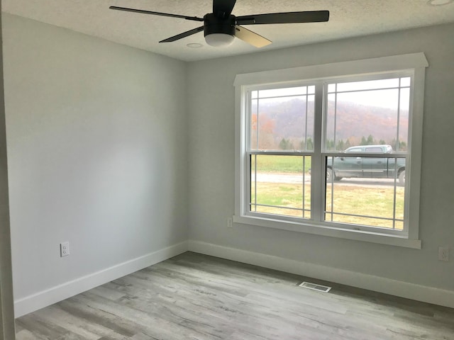 unfurnished room with a textured ceiling, light wood-type flooring, ceiling fan, and a healthy amount of sunlight