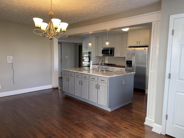 kitchen with appliances with stainless steel finishes, pendant lighting, a kitchen island with sink, and light stone counters