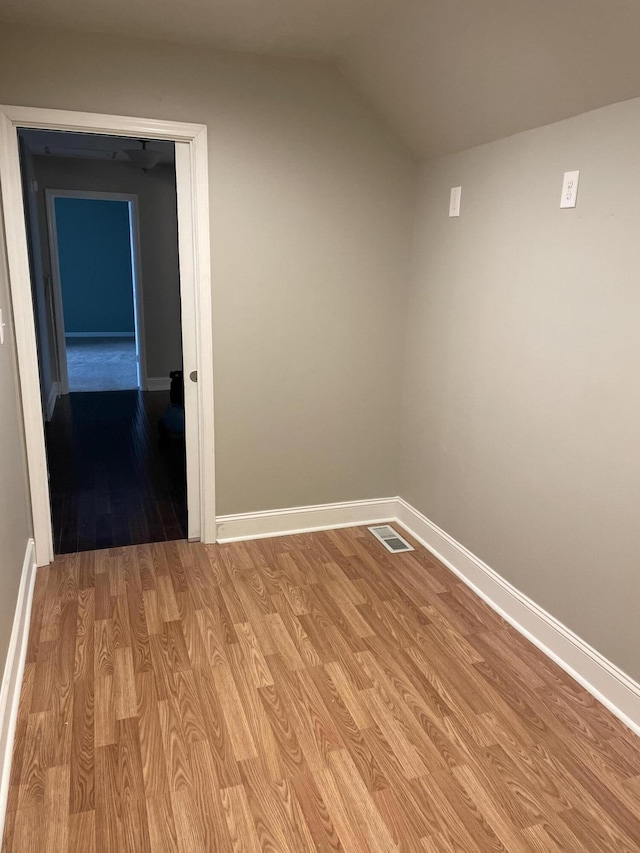 spare room featuring light wood-type flooring, visible vents, baseboards, and lofted ceiling