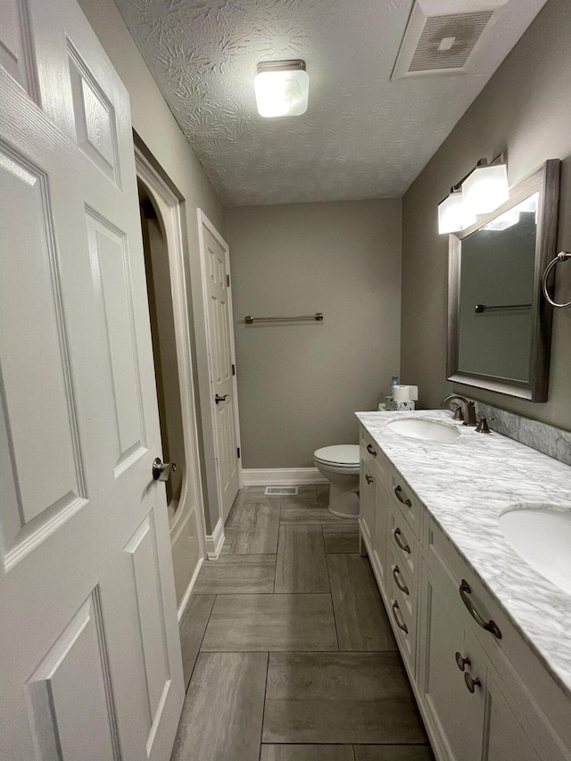 full bathroom featuring double vanity, visible vents, toilet, a sink, and a textured ceiling