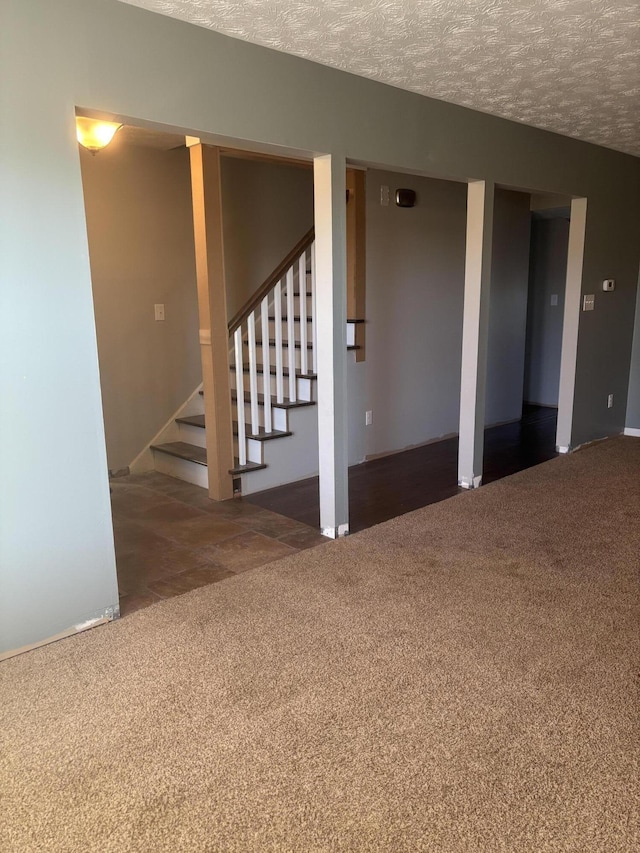 empty room featuring a textured ceiling, dark colored carpet, and stairway