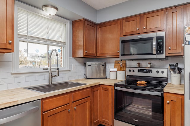 kitchen with stainless steel appliances, a sink, wooden counters, brown cabinets, and decorative backsplash