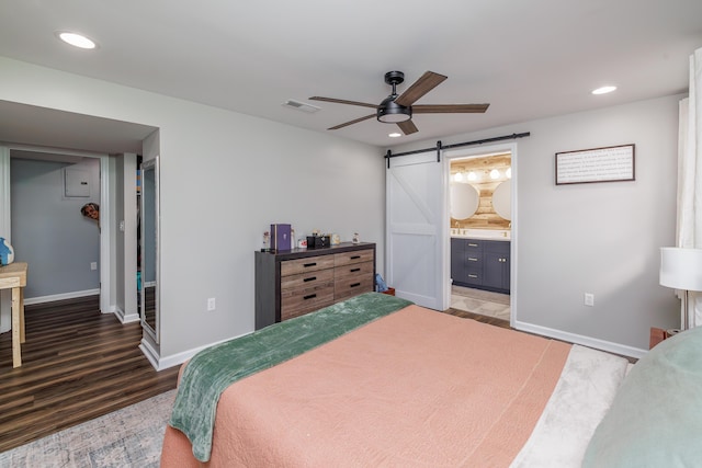 bedroom with a barn door, wood finished floors, baseboards, recessed lighting, and ensuite bathroom