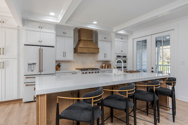 kitchen featuring appliances with stainless steel finishes, white cabinetry, a large island with sink, and custom exhaust hood