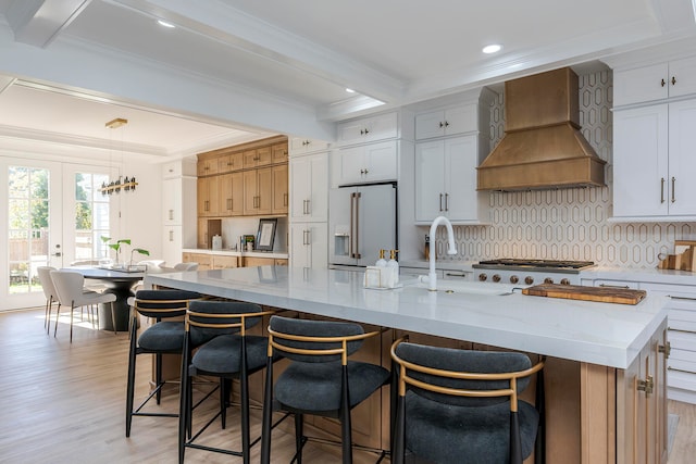 kitchen featuring pendant lighting, premium range hood, a spacious island, high end fridge, and white cabinetry